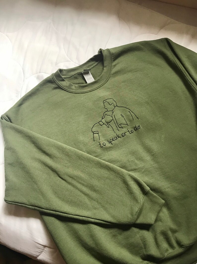 Puede incluir: Una sudadera verde con un dise&ntilde;o bordado en negro de dos figuras y el texto "to speak or to die".