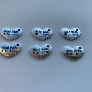 May include: Six silver heart-shaped charms with the text "Hand Made With Love" engraved on each charm.