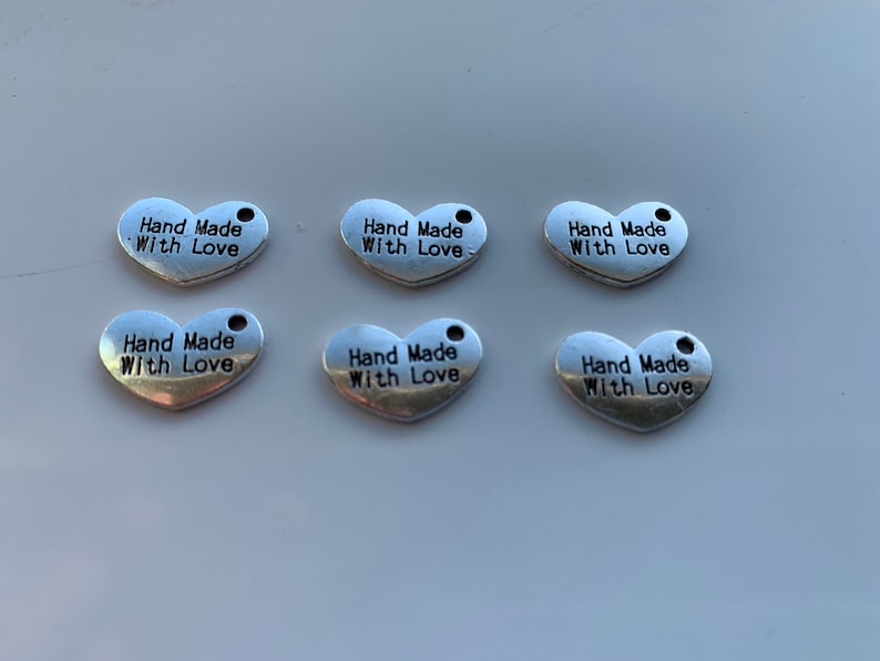 May include: Six silver heart-shaped charms with the text "Hand Made With Love" engraved on each charm.