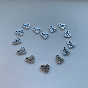 May include: A collection of silver heart-shaped charms with the words "Hand Made" printed on them.