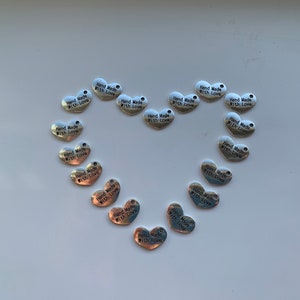 May include: A collection of silver heart-shaped charms with the text "Hand Made With Love" on each charm.