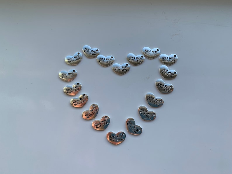 May include: A collection of silver heart-shaped charms with the text "Hand Made With Love" on each charm.