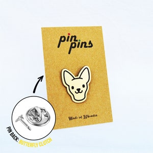 以下が含まれることがあります： 黒いアウトラインのクリーム色の犬の形をしたピン。茶色のカードに付いています。カードには黒で「pin pins」と「Made in Lithuania」と書かれています。ピンの裏側はバタフライクラッチです。