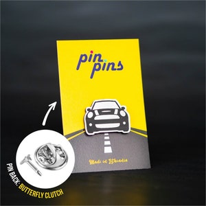 Op de afbeelding: Zwart-witte emaille pin van een Mini Cooper op een gele achtergrond met de tekst "pin pins" en "Made in Lithuania". De pin heeft een vlinder sluiting aan de achterkant.