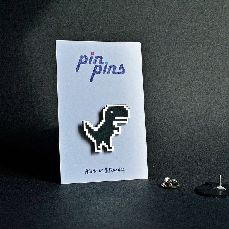 May include: Black pixelated dinosaur pin on a white card with the text "pin.pins" and "Made in Lithuania".