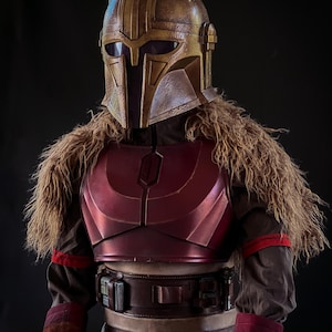 May include: A detailed costume featuring a gold and bronze helmet with a T-shaped visor, a burgundy chest plate, and a brown fur collar. The costume includes a brown belt with silver accents and brown sleeves with red trim.