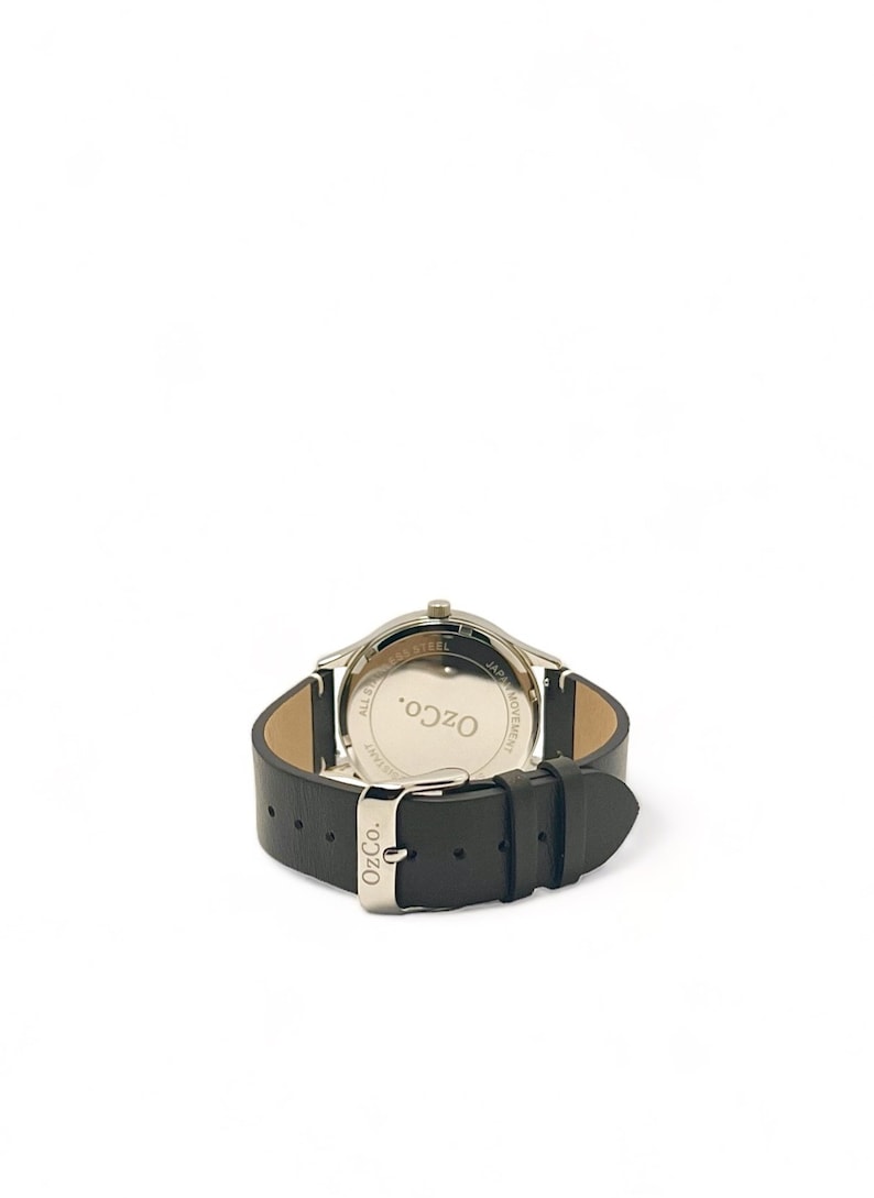 Pu&ograve; includere: Vista posteriore di un orologio argentato con cinturino in pelle nera. Il quadrante dell'orologio ha il testo "OzCo." e "All Stainless Steel" e "Japan Movement" stampato su di esso.