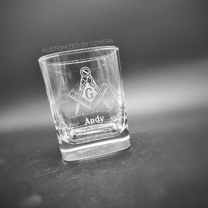 May include: Clear square-shaped glass with etched Masonic symbols and the name "Andy." The glass features a compass and square design, with the letter "G" in the center. The text "KUSTOMIZED BY COYERA" is above the glass.