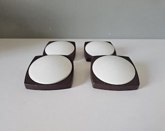 May include: A set of four square buttons, each featuring a dark brown frame with a smooth, raised white circular center. The buttons are arranged in a two-by-two grid, showcasing a clean, geometric design with contrasting colors and a matte finish.