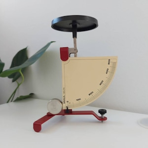 May include: A red and black scale with a circular platform and a graduated dial. The dial is marked with numbers from 0 to 500. The scale is labelled "MAUL DELTA".