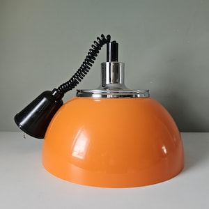 May include: Orange pendant light with a chrome base and a black cord. The light fixture has a rounded, dome-shaped shade. The cord is coiled and attached to a black socket.