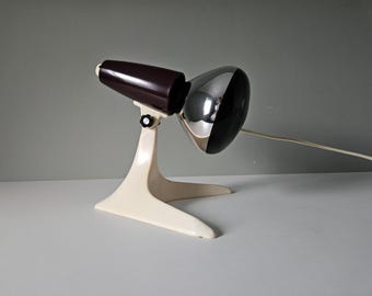 May include: A vintage desk lamp with a white base and a brown and chrome shade. The lamp has a flexible arm and a knob for adjusting the angle of the light.