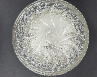 Könnte beinhalten: Runde, transparente Glasschale mit geprägtem floralem Muster. Die Schale hat einen gewellten Rand und ein spiralförmiges Design in der Mitte. Das Glas ist transparent und lässt Licht durch.