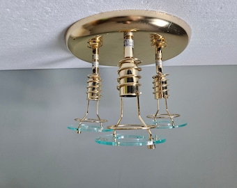 Könnte beinhalten: Eine goldene Deckenleuchte mit drei Glasschirmen. Die Leuchte hat eine runde, goldene Basis und drei hängende Leuchten mit goldenen Metallrahmen.