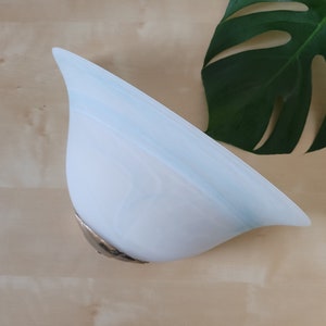 Könnte beinhalten: Eine weiße und blaue Glas-Wandleuchte in Tropfenform. Die Leuchte hat einen silberfarbenen Metallsockel und ein Wirbelmuster aus Weiß und Hellblau. Ein großes grünes Blatt befindet sich im Hintergrund.