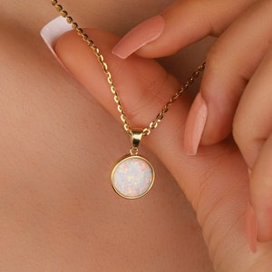 May include: A gold chain necklace with a round opal pendant. The pendant is white with a hint of pink and is set in a gold bezel.