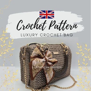 May include: A crocheted bag with a brown and gold chain strap and a decorative scarf tied to the handle. The bag is a neutral brown color and has a zipper closure. The text "Crochet Pattern" and "Luxury Crochet Bag" are displayed.