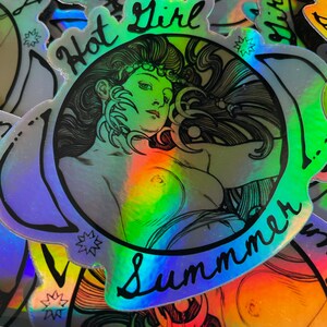 May include: Holographic sticker featuring a woman with long hair and the words "Hot Girl Summer" in a cursive font. The sticker has a rainbow sheen and a black outline. The image is a close-up of the sticker.