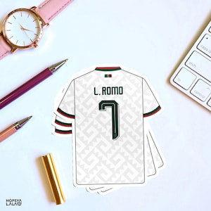 May include: A white soccer jersey sticker featuring a repeating light gray geometric pattern, the name L. ROMO, and the number 7 in dark green. The jersey has dark green and red trim on the sleeves and collar, with a small Mexican flag icon.