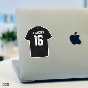 May include: A black sports jersey sticker featuring the name J. QUI&Ntilde;ONES and the number 16 in white lettering. The jersey has a subtle dark geometric pattern, a small green and red detail at the collar, and a white border outline.