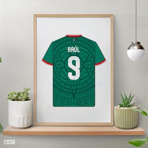 May include: A framed print featuring a green soccer jersey with a dark green Aztec-inspired circular pattern. The jersey displays the name RA&Uacute;L and the number 9 in white, with red and white trim on the sleeves and collar, presented in a light wood frame.