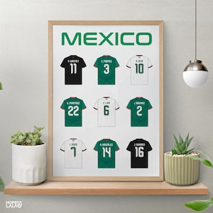 May include: A framed poster titled MEXICO featuring nine soccer jerseys arranged in a grid. The jerseys are black, green, and white, each displaying a player name and number on the back. The print is displayed in a light wood frame on a shelf.