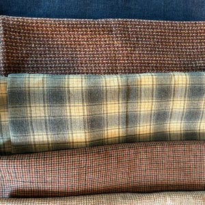 May include: An assortment of fabric swatches in various patterns and colors. The top swatch is a dark blue denim. Below are brown, plaid, and patterned fabrics in shades of red, gray, and beige.