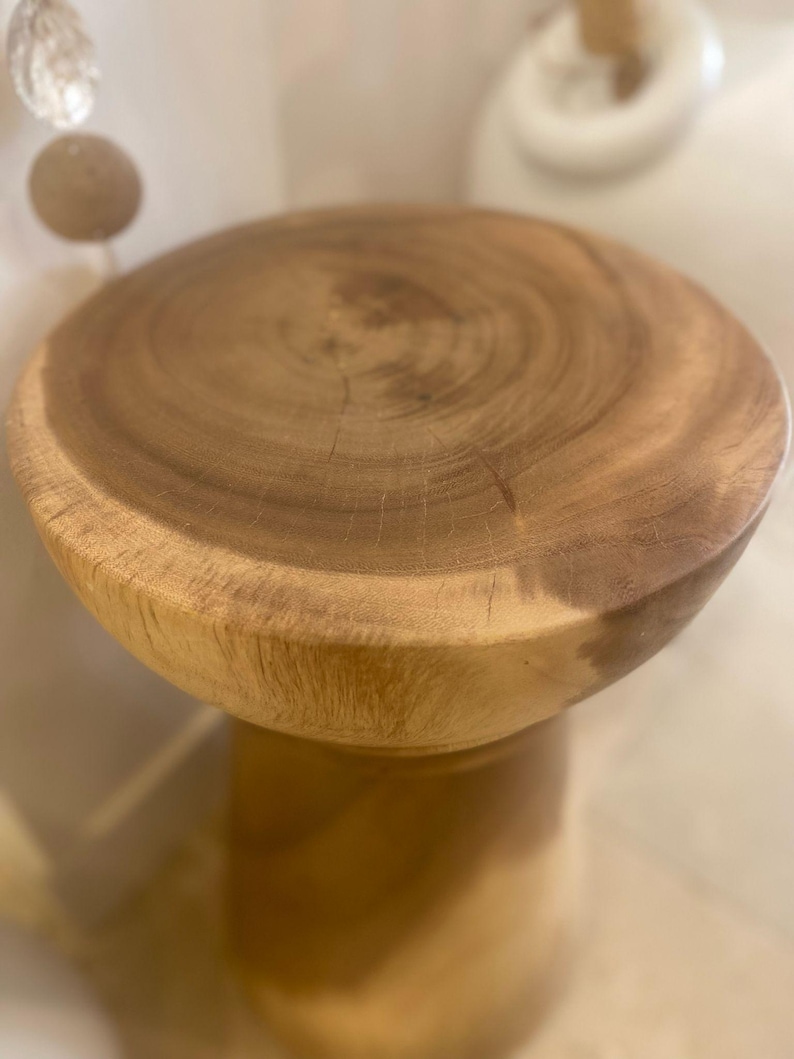 May include: A round wooden stool featuring a natural light brown finish with visible wood grain patterns on the circular top surface. The stool has a smooth, polished texture and a solid, cylindrical base that tapers slightly toward the center.
