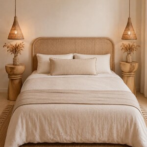 May include: A bed featuring a rounded rattan headboard, white bedding, a beige lumbar pillow, and a matching bed runner. Two wooden side tables hold vases with dried flowers, flanked by two hanging cone-shaped woven pendant lights.