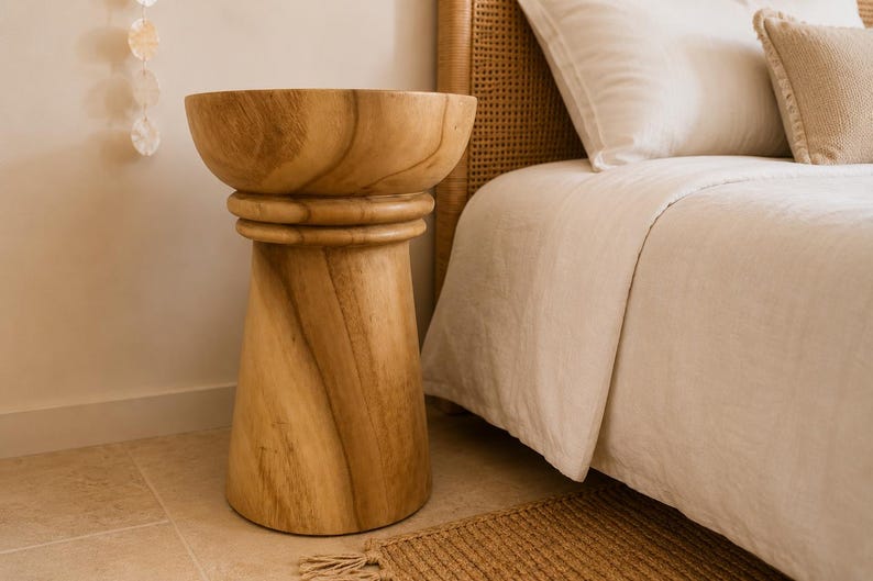May include: A light brown wooden side table with a smooth, circular top and a tapered, cylindrical base. The table features a distinct horizontal ring detail just below the top surface, showcasing the natural wood grain patterns throughout the piece.