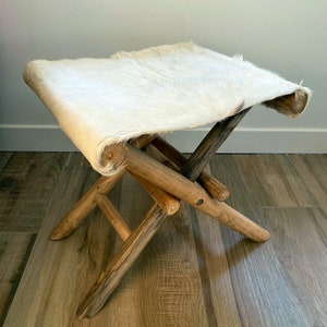 Peut inclure: Un tabouret pliant recouvert de fourrure blanche avec une structure en bois. Le tabouret est fait de matériaux naturels et a un aspect rustique.