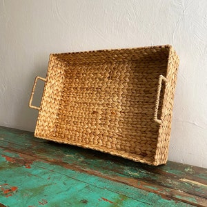 Op de afbeelding: Een rechthoekige geweven dienblad met twee handvatten. Het dienblad is gemaakt van natuurlijk geweven materiaal en heeft een lichtbruine kleur.