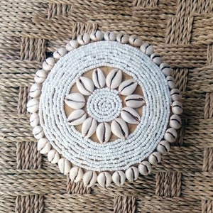 Peut inclure: Un dessous de verre circulaire en petites perles blanches et coquillages. Le dessous de verre a un motif central de fleur avec un cercle de perles au centre.