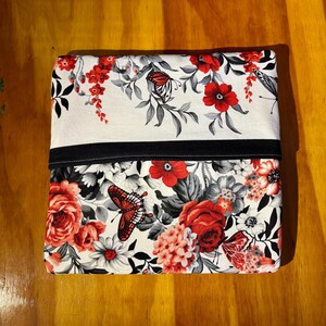 May include: A rectangular pillowcase with a floral and butterfly pattern. The top section is white with red flowers and butterflies, separated by a black band from the bottom section, which has a similar design.
