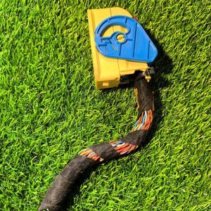 Pode incluir: Um conector elétrico automotivo amarelo e azul com um feixe de fios preto. O conector tem uma alça azul e está sobre um fundo verde.