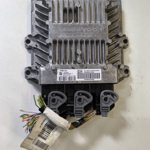 May include: A silver Siemens VDO automotive computer module with a ribbed top and three black connectors. Attached are multi-coloured wires and a label with text and a barcode. The module is on a white surface.