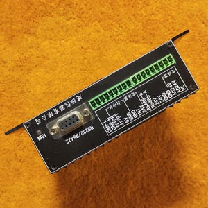 May include: A black electronic device with a variety of ports and connectors, including RS232/RS422, CAN-L, CAN-H, Print R, Print T, 5V, GND, INT, 24V, AC24V, and PE. The device has a green terminal block with multiple pins. The text "建恒仪器有限公司" is printed on the device.