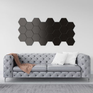 Könnte beinhalten: Ein graues, gestepptes Sofa mit einer braunen Wolldecke und einem weißen Kissen. Das Sofa steht vor einer weißen Wand mit einem schwarzen geometrischen Wandbild.