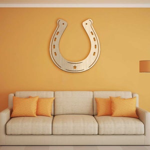 May include: A beige sofa with two orange throw pillows in front of a yellow wall with a large wooden horseshoe cutout hanging on the wall. A floor lamp with a brown lampshade is in the corner of the room.