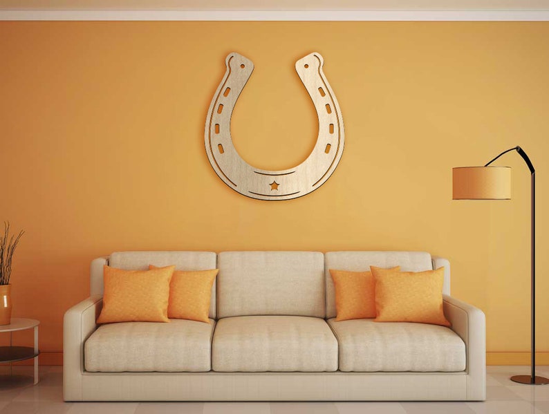 May include: A beige sofa with two orange throw pillows in front of a yellow wall with a large wooden horseshoe cutout hanging on the wall. A floor lamp with a brown lampshade is in the corner of the room.