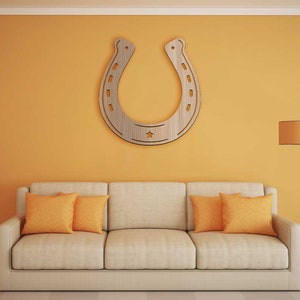 May include: A beige sofa with two orange throw pillows sits in front of a yellow wall with a large wooden horseshoe cutout hanging on the wall. A floor lamp with a brown lampshade is in the corner of the room.