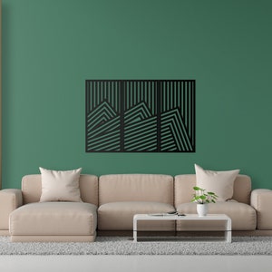 May include: A black geometric wall art piece with a mountain range design. The art is made of metal and has a modern style. It is hanging on a green wall in a living room setting.