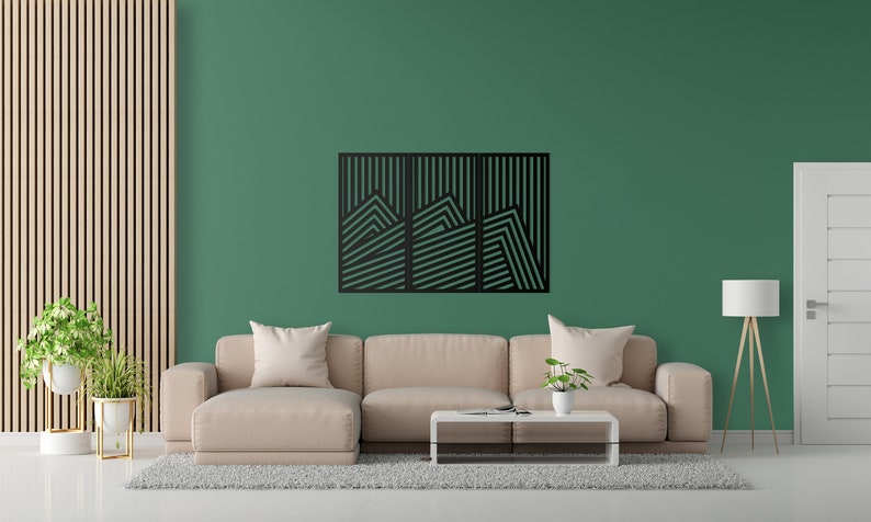 May include: A black geometric wall art piece with a mountain range design. The art is made of metal and has a modern style. It is hanging on a green wall in a living room setting.
