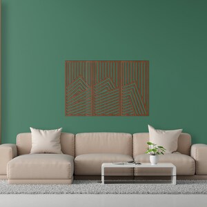 May include: A light brown sectional sofa with three cushions sits in front of a green wall with a wooden geometric wall art piece. A small potted plant sits on a coffee table in front of the sofa. A floor lamp with a white lampshade stands next to a white door.