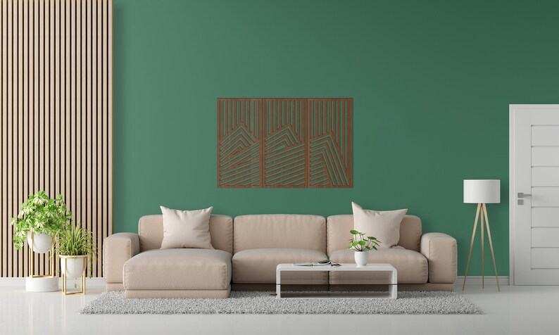 May include: A light brown sectional sofa with three cushions sits in front of a green wall with a wooden geometric wall art piece. A small potted plant sits on a coffee table in front of the sofa. A floor lamp with a white lampshade stands next to a white door.