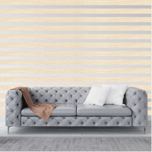 May include: A gray tufted sofa with a brown throw blanket and two white pillows in front of a wall with horizontal wood paneling.