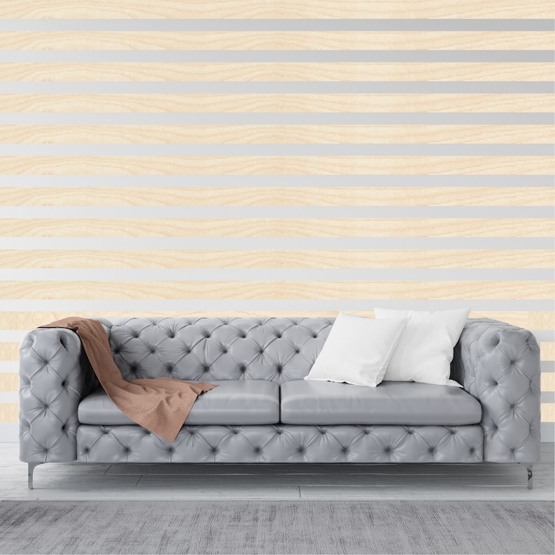 May include: A gray tufted sofa with a brown throw blanket and two white pillows in front of a wall with horizontal wood paneling.