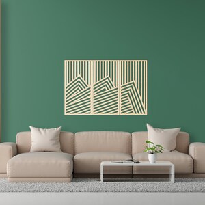 May include: A living room interior with a beige sectional sofa, a coffee table, and a three-piece wooden wall art with a geometric design. The wall art is made of light wood and features a series of horizontal lines that create a mountain-like pattern. The wall is painted a deep green colour.