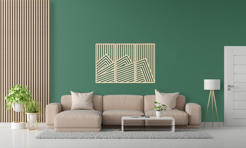 May include: A living room interior with a beige sectional sofa, a coffee table, and a three-piece wooden wall art with a geometric design. The wall art is made of light wood and features a series of horizontal lines that create a mountain-like pattern. The wall is painted a deep green colour.