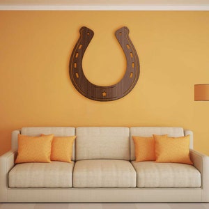 May include: A beige sofa with three orange throw pillows sits in front of a yellow wall with a large wooden horseshoe hanging on it. A floor lamp with a round lampshade is in the corner of the room.